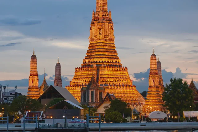 Wat Arun illuminated beside the Chao Phraya River at dusk